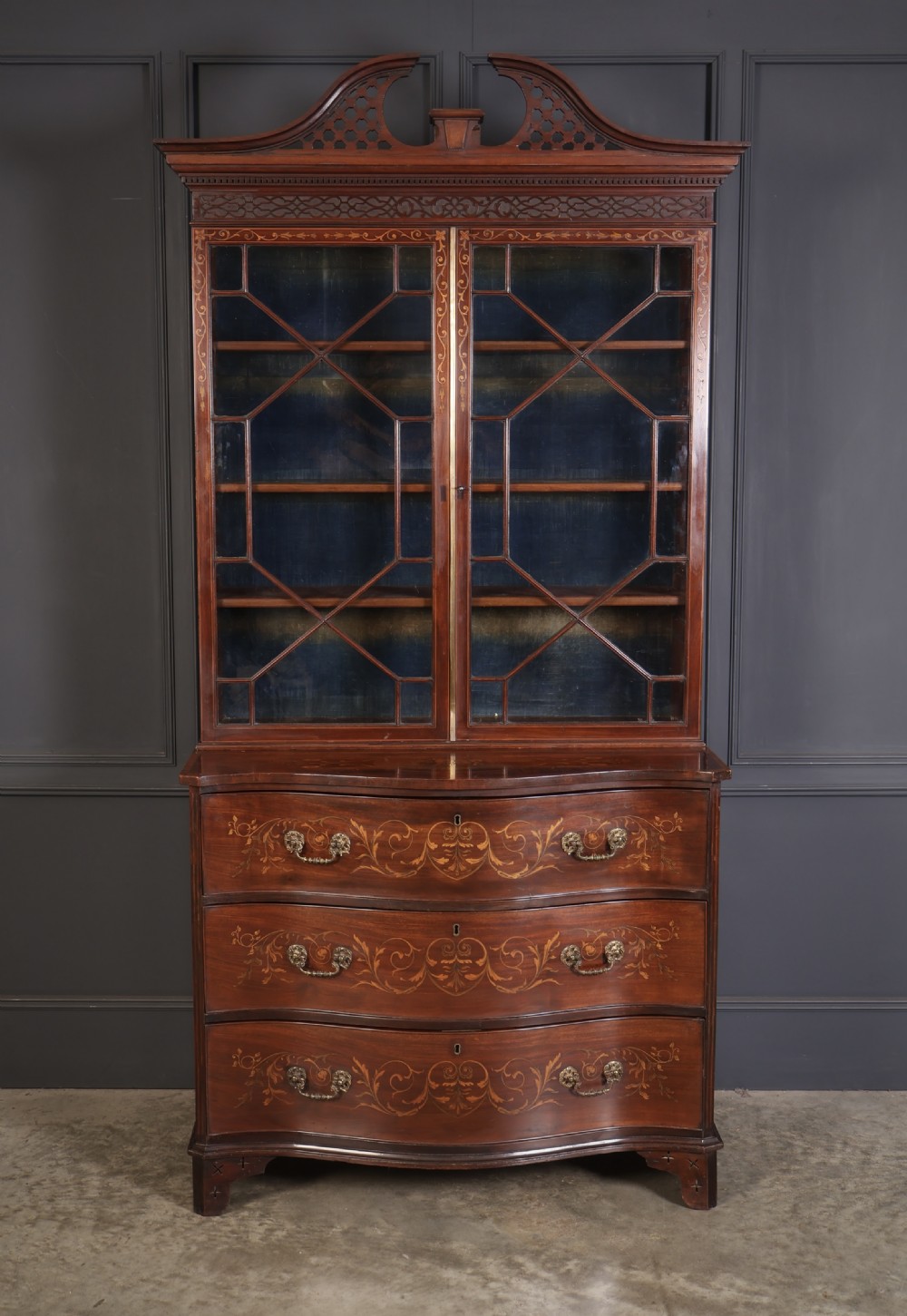 A tall Georgian mahogany bookcase featuring a pierced fretwork pediment, two upper glazed doors with intricate geometric glazing bars, and a lower serpentine chest of three drawers adorned with detailed floral marquetry inlays and brass handles. View II