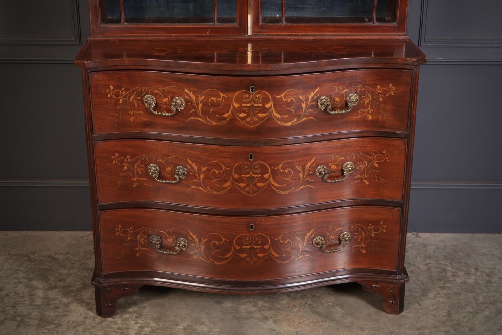 A tall Georgian mahogany bookcase featuring a pierced fretwork pediment, two upper glazed doors with intricate geometric glazing bars, and a lower serpentine chest of three drawers adorned with detailed floral marquetry inlays and brass handles. View III