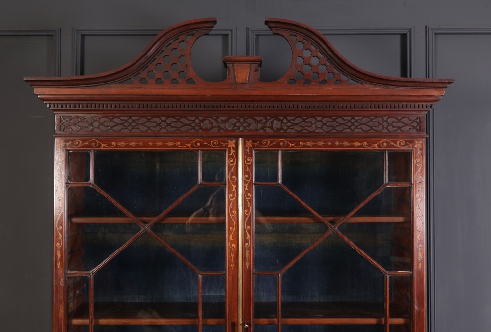 A tall Georgian mahogany bookcase featuring a pierced fretwork pediment, two upper glazed doors with intricate geometric glazing bars, and a lower serpentine chest of three drawers adorned with detailed floral marquetry inlays and brass handles. View IV
