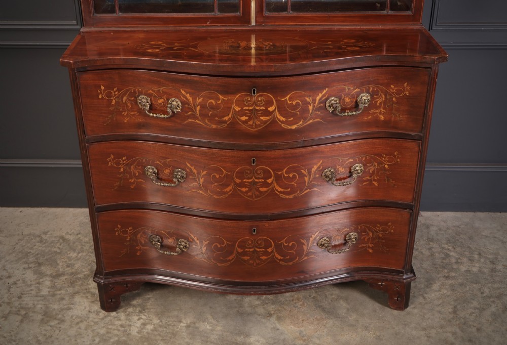 A tall Georgian mahogany bookcase featuring a pierced fretwork pediment, two upper glazed doors with intricate geometric glazing bars, and a lower serpentine chest of three drawers adorned with detailed floral marquetry inlays and brass handles. View V