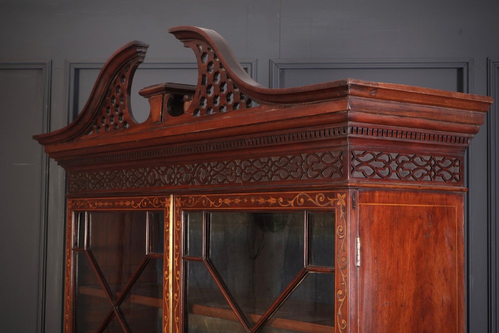 A tall Georgian mahogany bookcase featuring a pierced fretwork pediment, two upper glazed doors with intricate geometric glazing bars, and a lower serpentine chest of three drawers adorned with detailed floral marquetry inlays and brass handles. View VIII