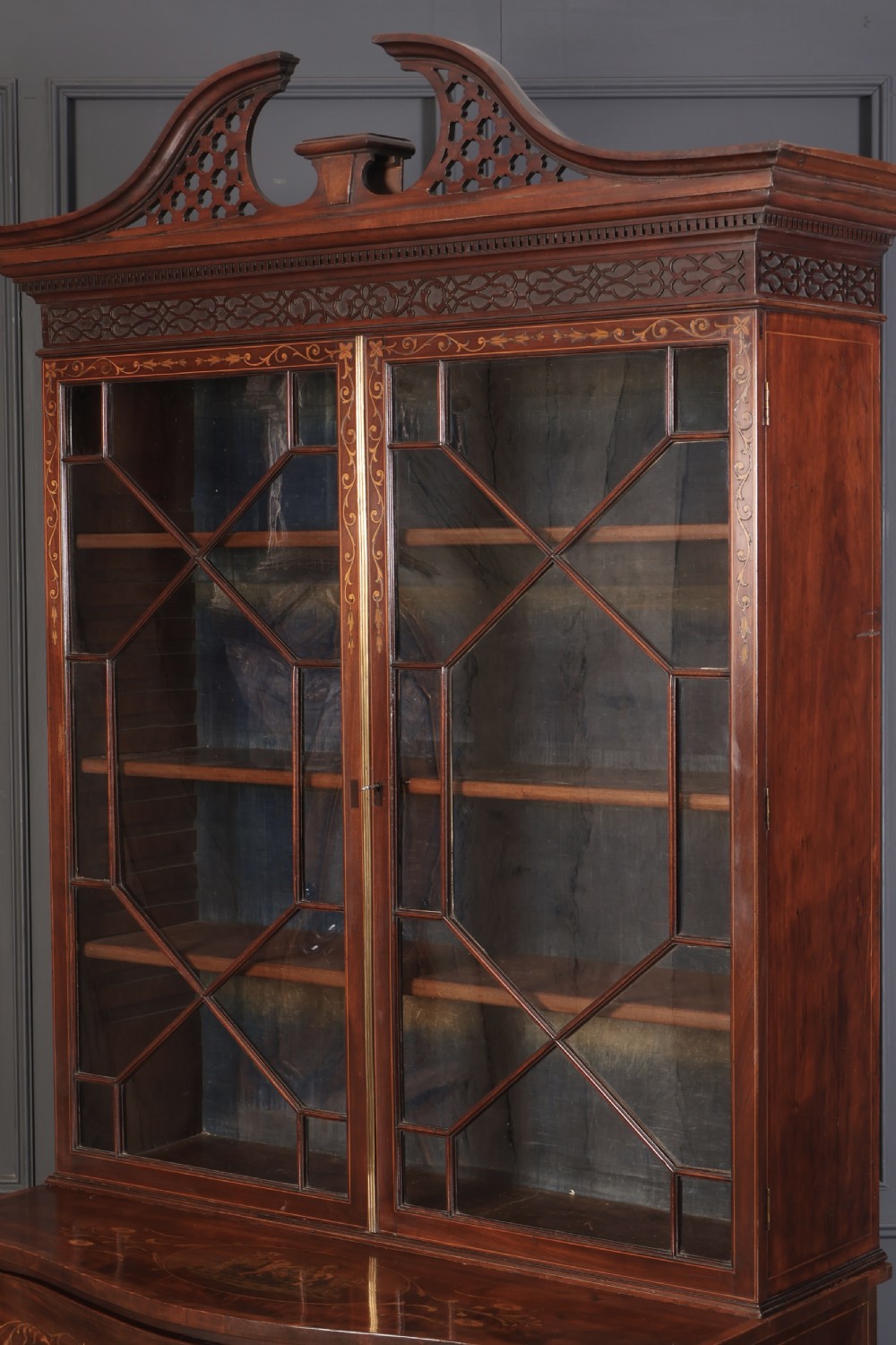 A tall Georgian mahogany bookcase featuring a pierced fretwork pediment, two upper glazed doors with intricate geometric glazing bars, and a lower serpentine chest of three drawers adorned with detailed floral marquetry inlays and brass handles. View X