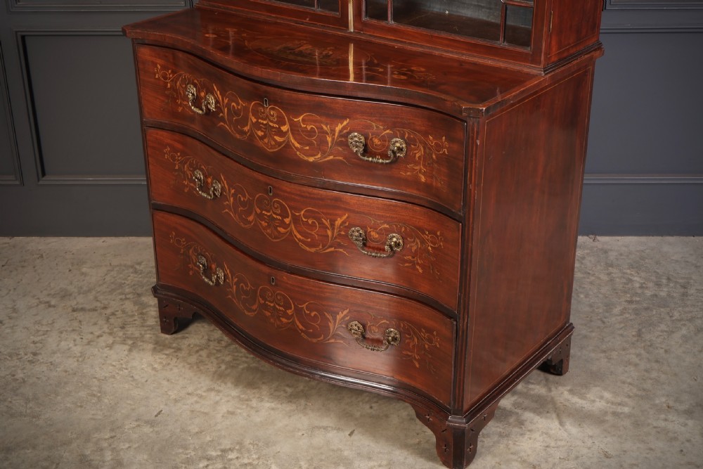 A tall Georgian mahogany bookcase featuring a pierced fretwork pediment, two upper glazed doors with intricate geometric glazing bars, and a lower serpentine chest of three drawers adorned with detailed floral marquetry inlays and brass handles. View XII