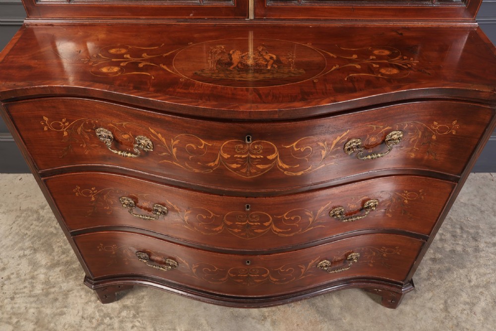 A tall Georgian mahogany bookcase featuring a pierced fretwork pediment, two upper glazed doors with intricate geometric glazing bars, and a lower serpentine chest of three drawers adorned with detailed floral marquetry inlays and brass handles. View XVII