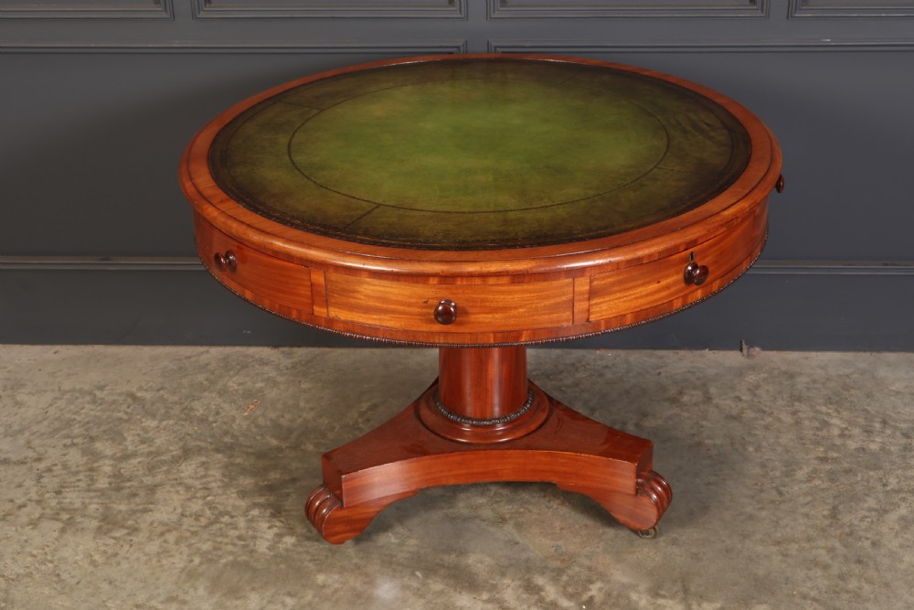 A Victorian circular mahogany drum table featuring a green leather inset top, perimeter frieze drawers with wooden knobs, and a central pedestal base with castors.