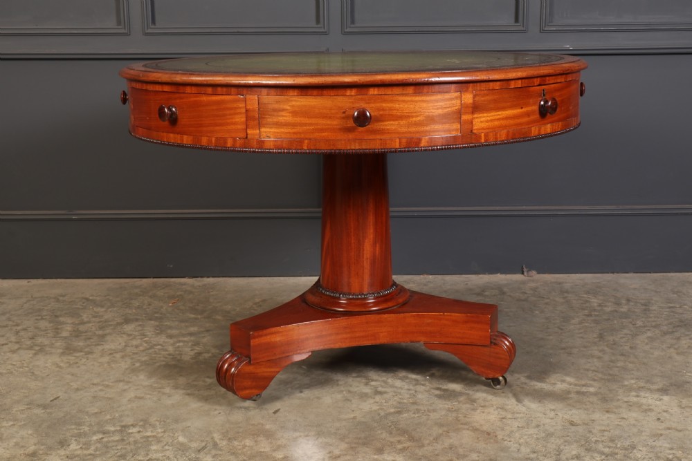 A Victorian circular mahogany drum table featuring a green leather inset top, perimeter frieze drawers with wooden knobs, and a central pedestal base with castors. View VII