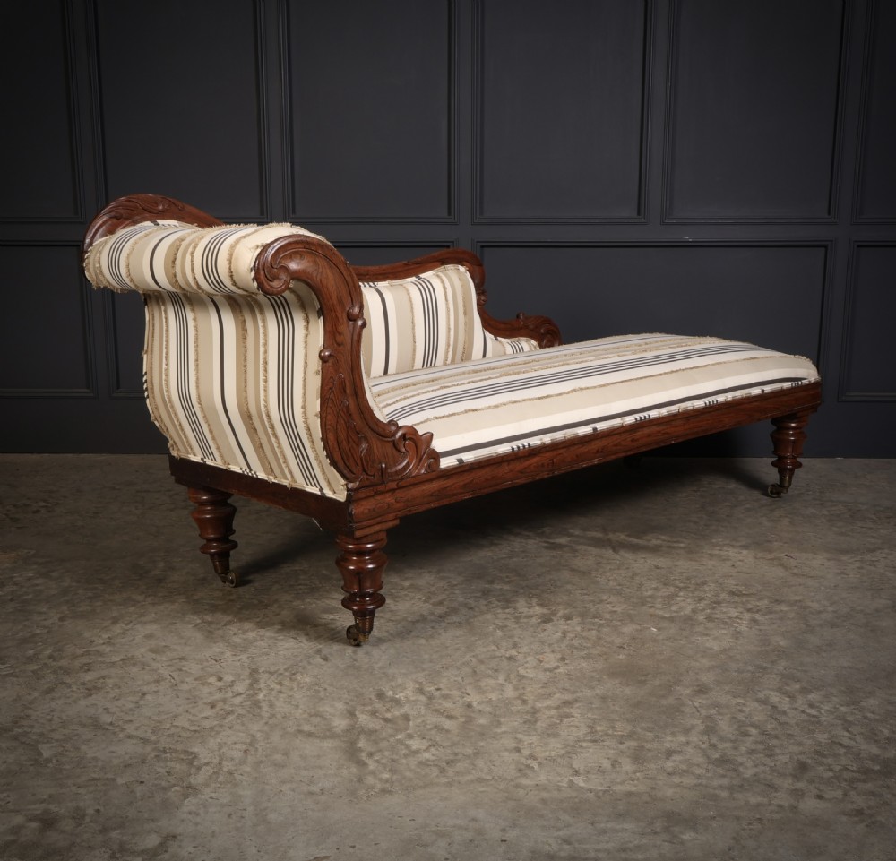 A William IV rosewood chaise longue featuring an asymmetrical scrolled backrest, striped cream and brown fabric upholstery, carved floral accents, turned legs, and brass castors.