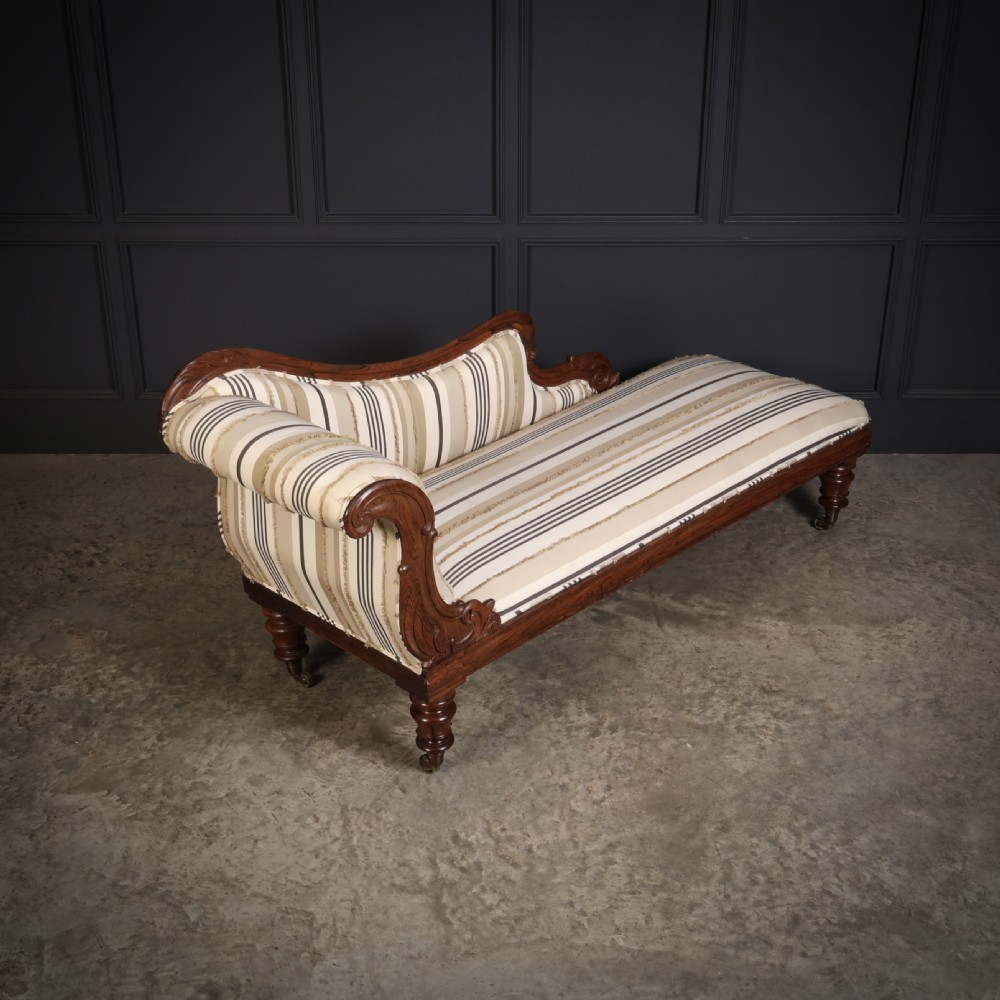 A William IV rosewood chaise longue featuring an asymmetrical scrolled backrest, striped cream and brown fabric upholstery, carved floral accents, turned legs, and brass castors. View II