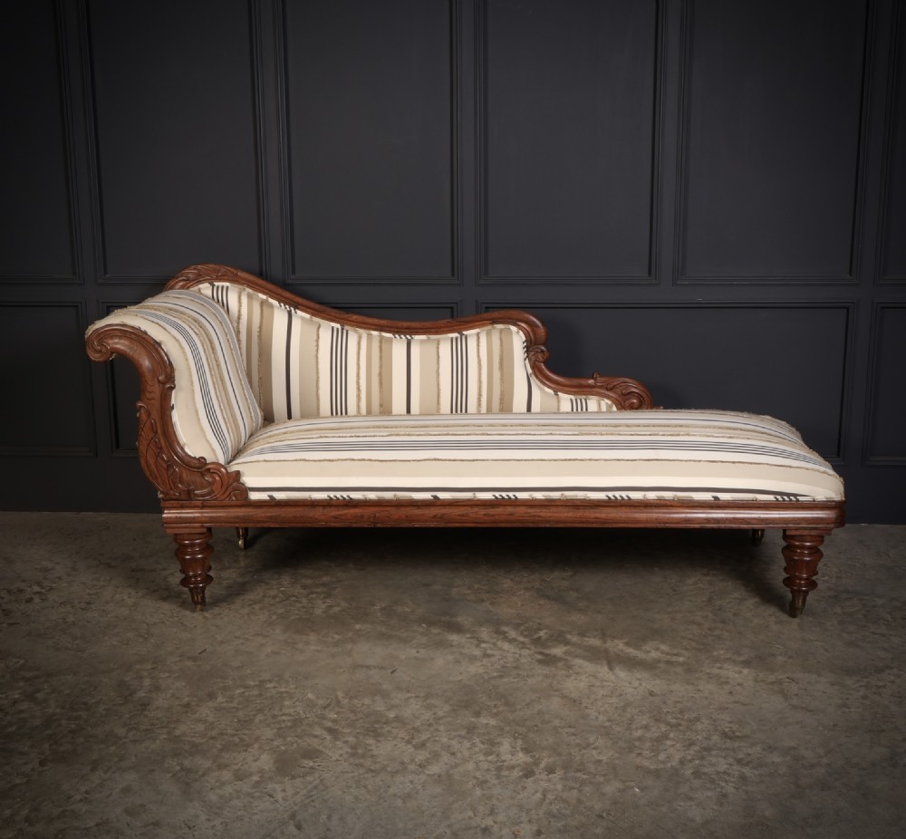 A William IV rosewood chaise longue featuring an asymmetrical scrolled backrest, striped cream and brown fabric upholstery, carved floral accents, turned legs, and brass castors. View III