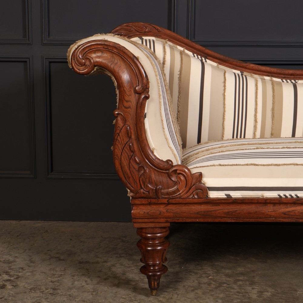 A William IV rosewood chaise longue featuring an asymmetrical scrolled backrest, striped cream and brown fabric upholstery, carved floral accents, turned legs, and brass castors. View V
