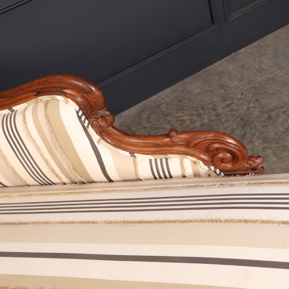 A William IV rosewood chaise longue featuring an asymmetrical scrolled backrest, striped cream and brown fabric upholstery, carved floral accents, turned legs, and brass castors. View IX
