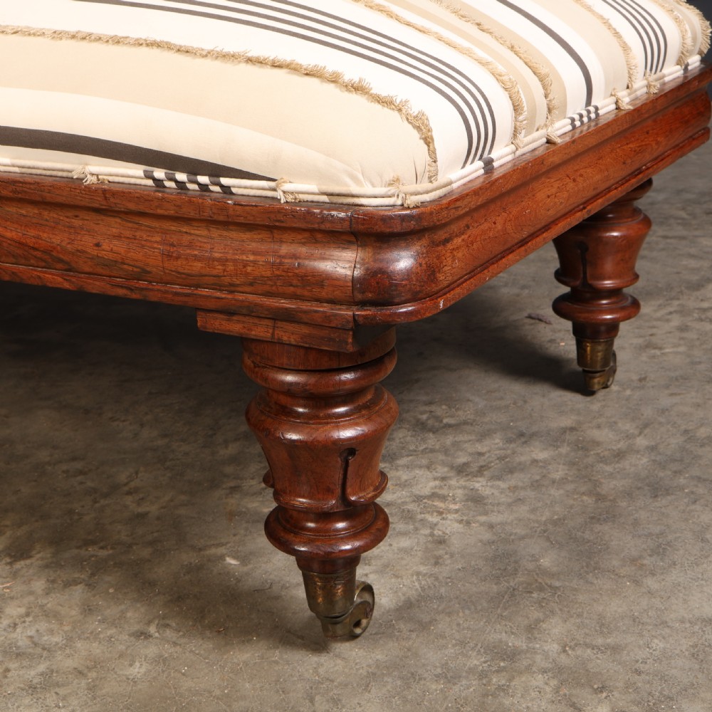 A William IV rosewood chaise longue featuring an asymmetrical scrolled backrest, striped cream and brown fabric upholstery, carved floral accents, turned legs, and brass castors. View X