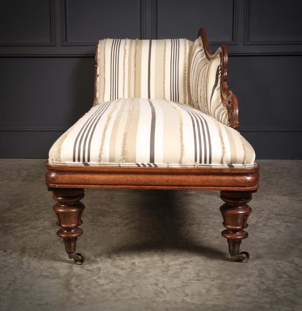 A William IV rosewood chaise longue featuring an asymmetrical scrolled backrest, striped cream and brown fabric upholstery, carved floral accents, turned legs, and brass castors. View XI