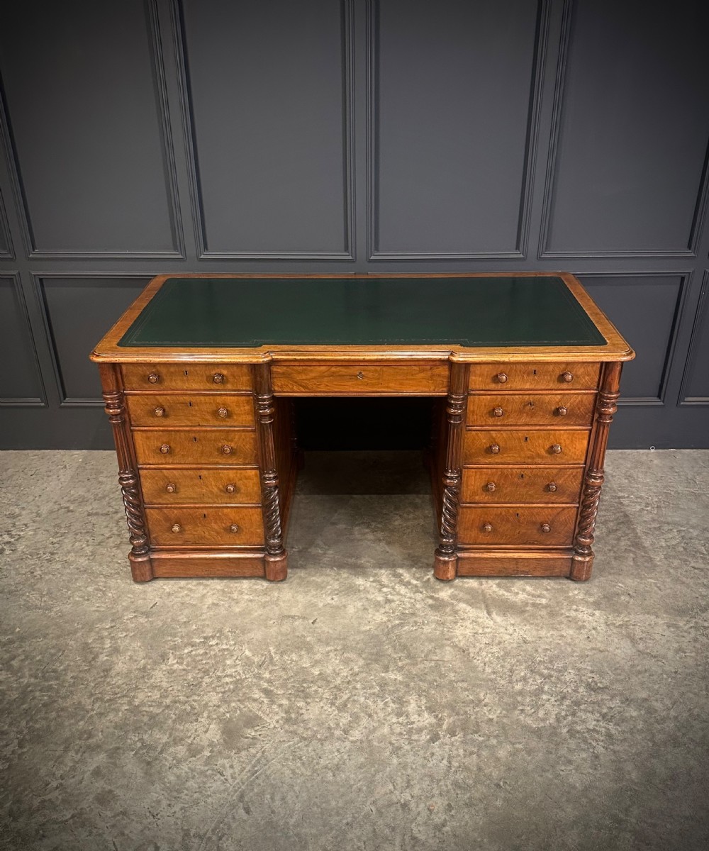 A Victorian figured walnut pedestal desk featuring a green leather writing surface, turned drawer knobs, and carved barley twist pilasters.