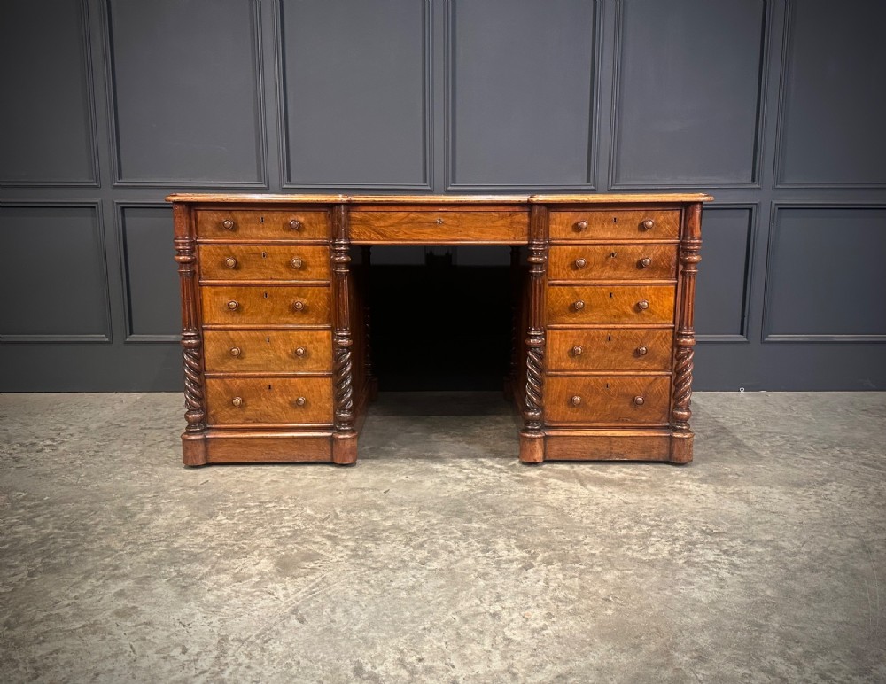 A Victorian figured walnut pedestal desk featuring a green leather writing surface, turned drawer knobs, and carved barley twist pilasters. View IV