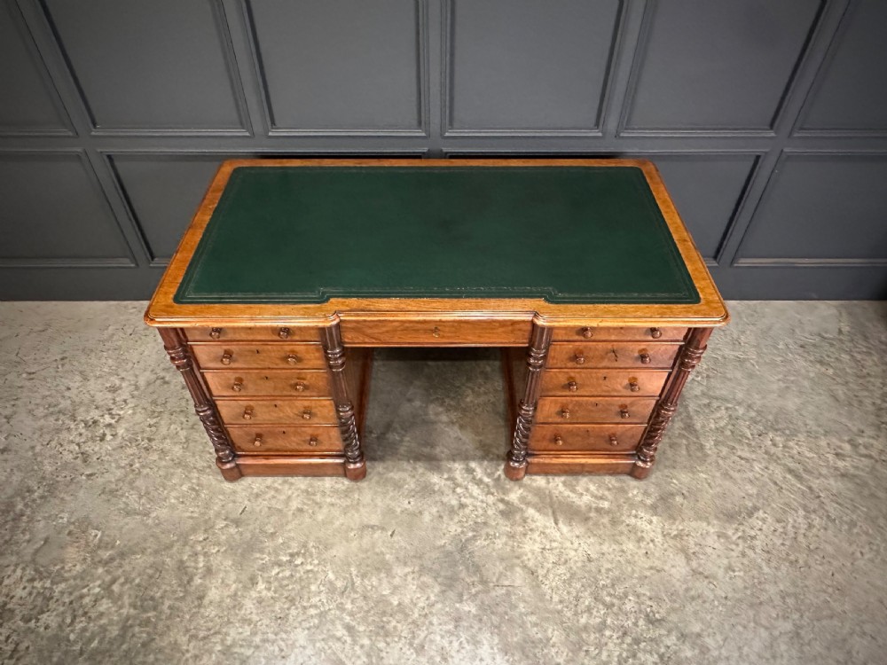 A Victorian figured walnut pedestal desk featuring a green leather writing surface, turned drawer knobs, and carved barley twist pilasters. View V