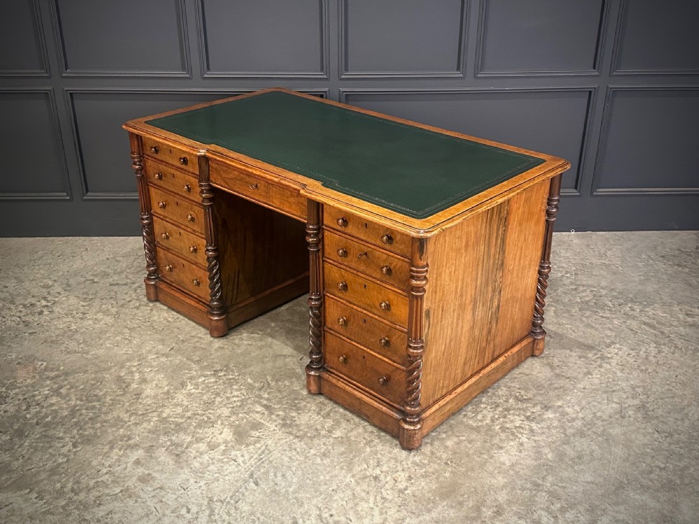 A Victorian figured walnut pedestal desk featuring a green leather writing surface, turned drawer knobs, and carved barley twist pilasters. View VI