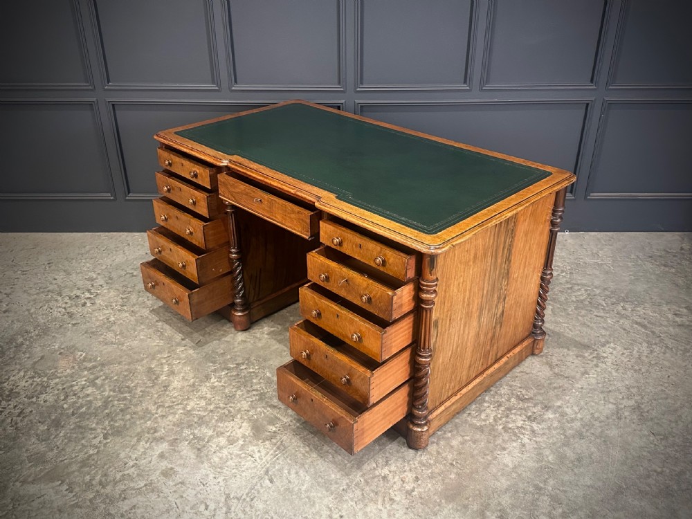 A Victorian figured walnut pedestal desk featuring a green leather writing surface, turned drawer knobs, and carved barley twist pilasters. View VIII