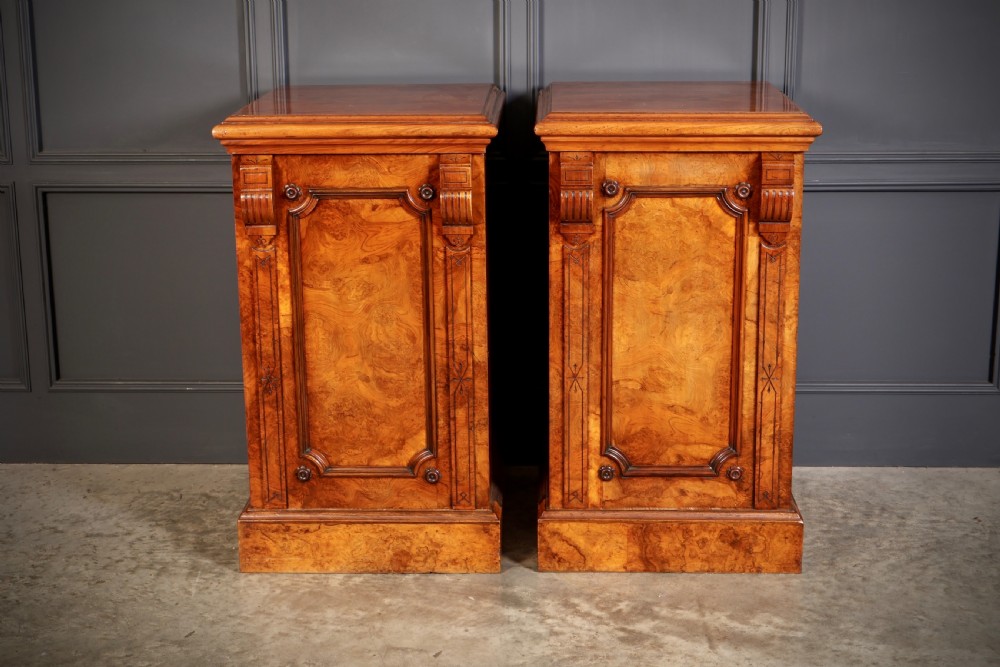 A matching pair of Victorian figured walnut pedestal cabinets featuring carved corbels, panelled doors with decorative line inlay, and sturdy plinth bases.