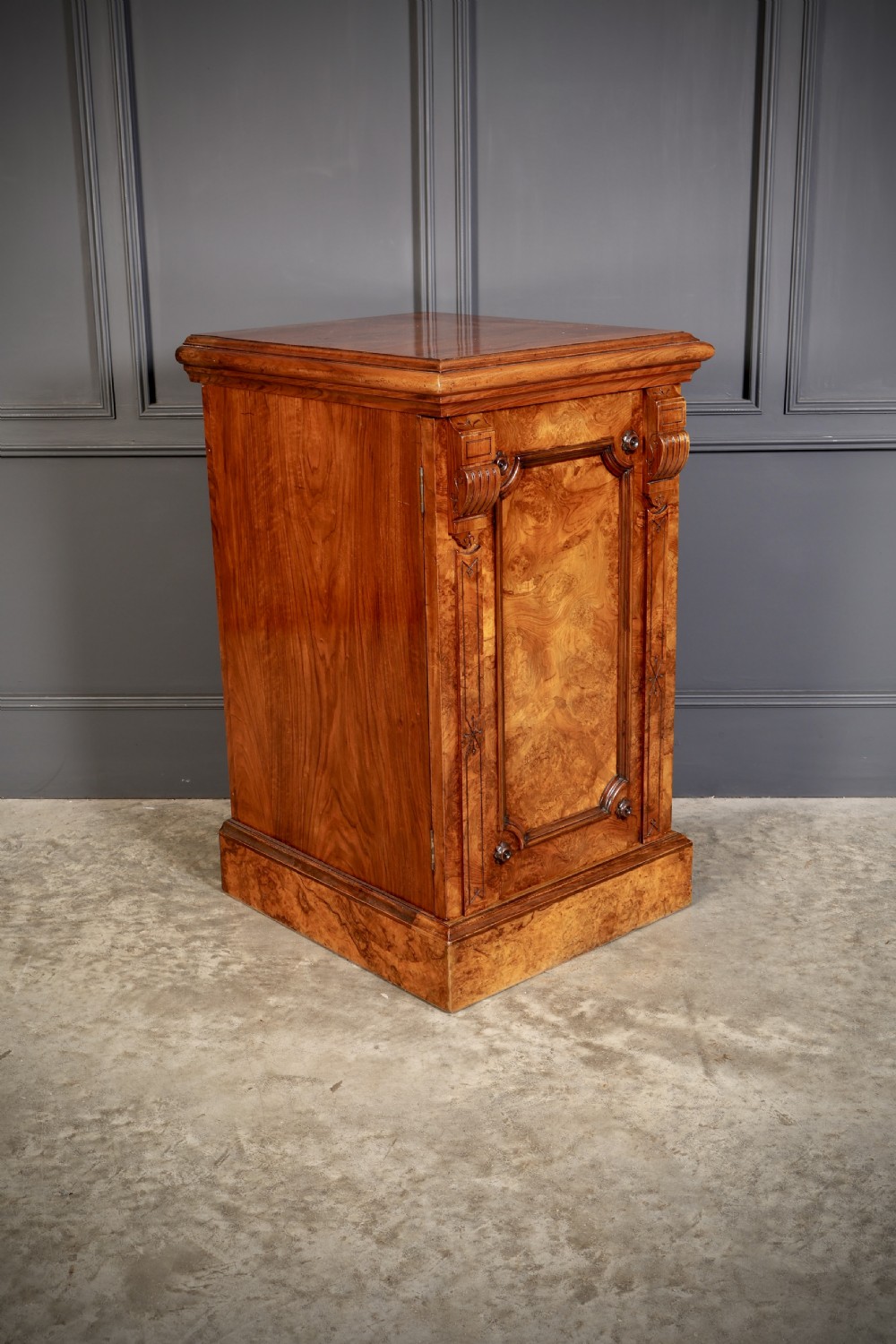 A matching pair of Victorian figured walnut pedestal cabinets featuring carved corbels, panelled doors with decorative line inlay, and sturdy plinth bases. View V