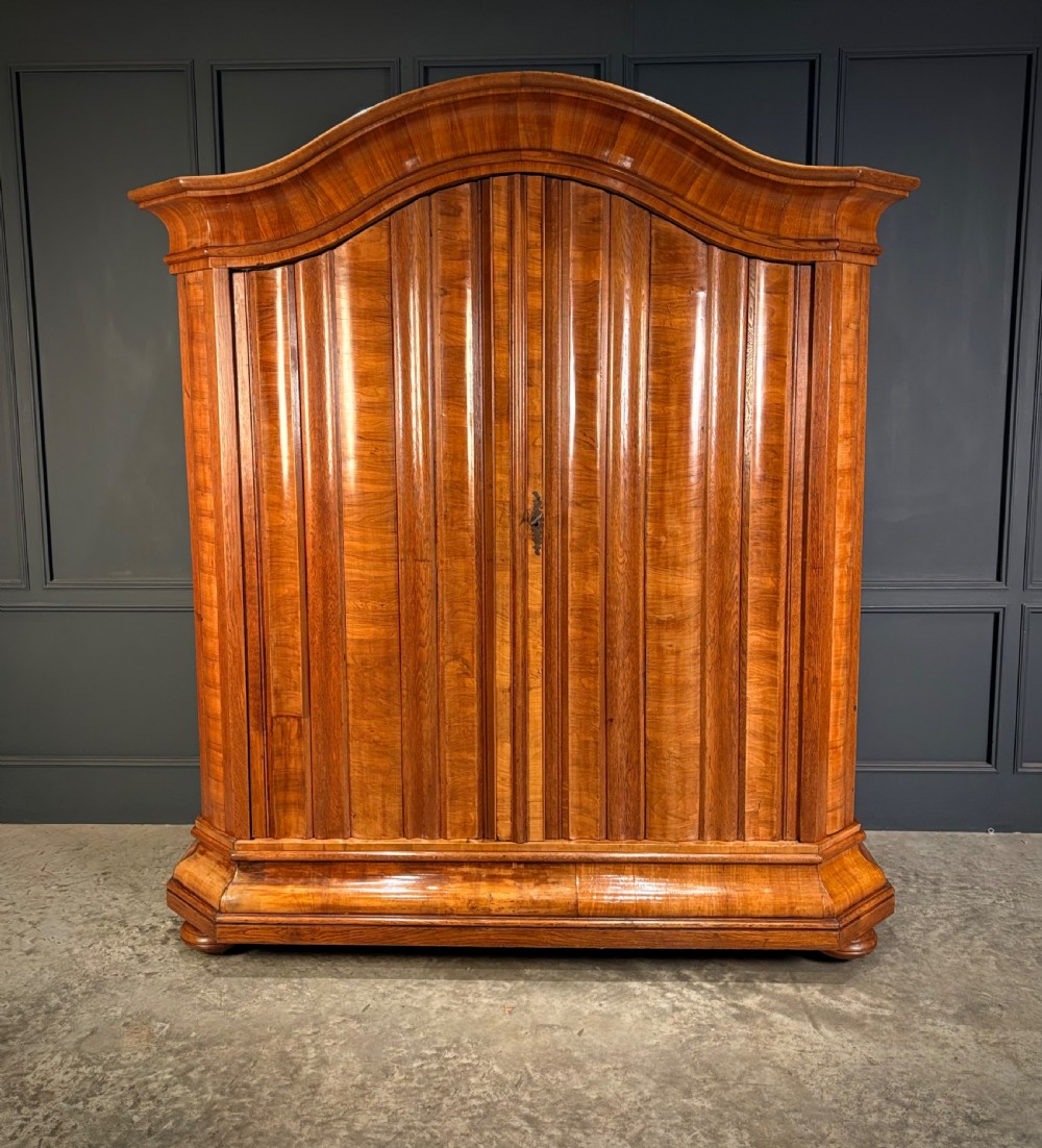A large Continental oak and walnut armoire featuring a curved arched pediment, vertical fluted double doors, and a moulded plinth base.