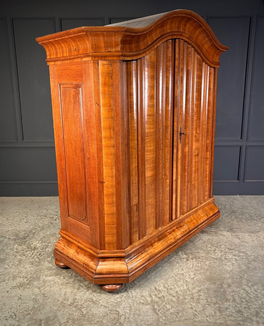 A large Continental oak and walnut armoire featuring a curved arched pediment, vertical fluted double doors, and a moulded plinth base. View II