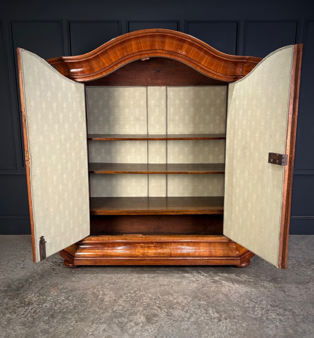 A large Continental oak and walnut armoire featuring a curved arched pediment, vertical fluted double doors, and a moulded plinth base. View III