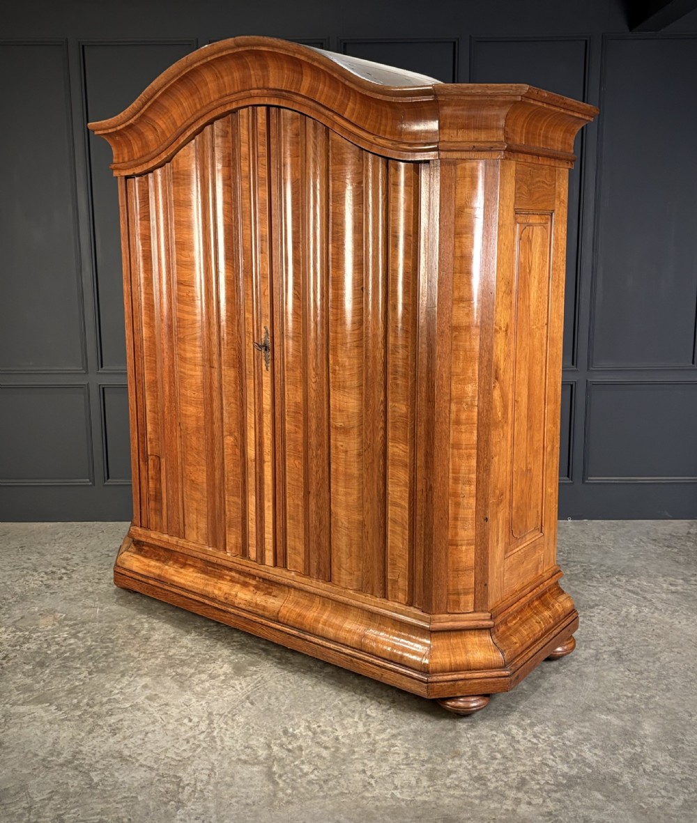 A large Continental oak and walnut armoire featuring a curved arched pediment, vertical fluted double doors, and a moulded plinth base. View IV