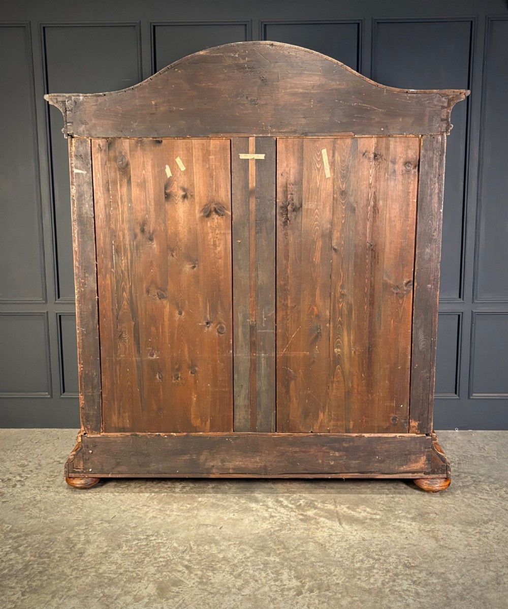 A large Continental oak and walnut armoire featuring a curved arched pediment, vertical fluted double doors, and a moulded plinth base. View VI
