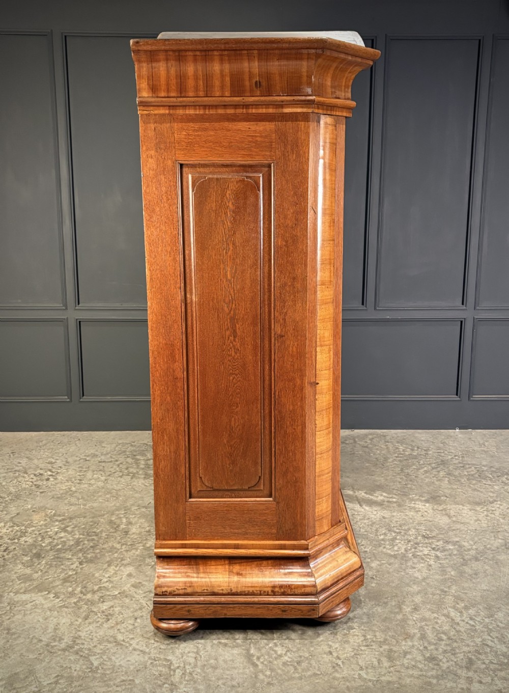 A large Continental oak and walnut armoire featuring a curved arched pediment, vertical fluted double doors, and a moulded plinth base. View VII