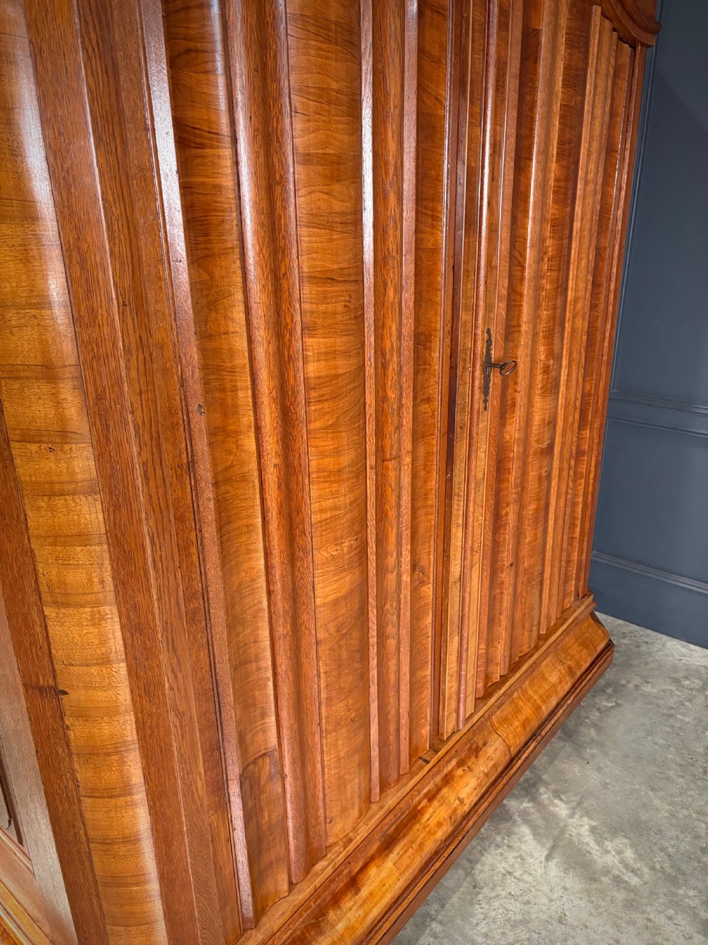 A large Continental oak and walnut armoire featuring a curved arched pediment, vertical fluted double doors, and a moulded plinth base. View IX