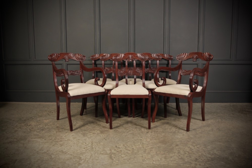 A set of eight carved mahogany Regency dining chairs featuring scroll arms, carved crest rails, and cream upholstered seats. View III