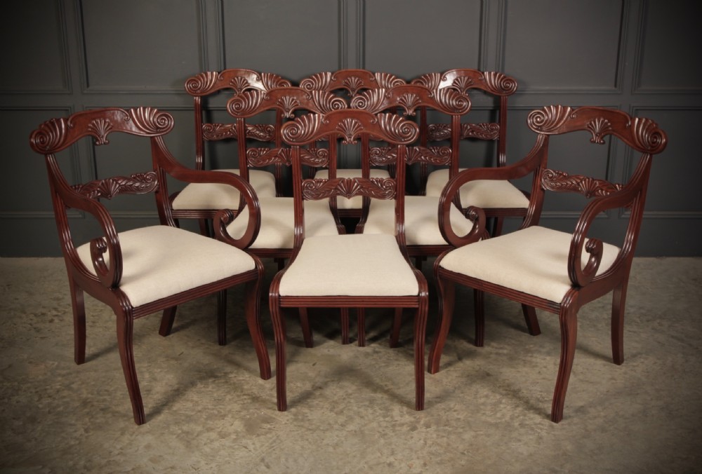 A set of eight carved mahogany Regency dining chairs featuring scroll arms, carved crest rails, and cream upholstered seats. View II