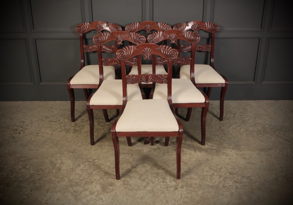 A set of eight carved mahogany Regency dining chairs featuring scroll arms, carved crest rails, and cream upholstered seats. View IV