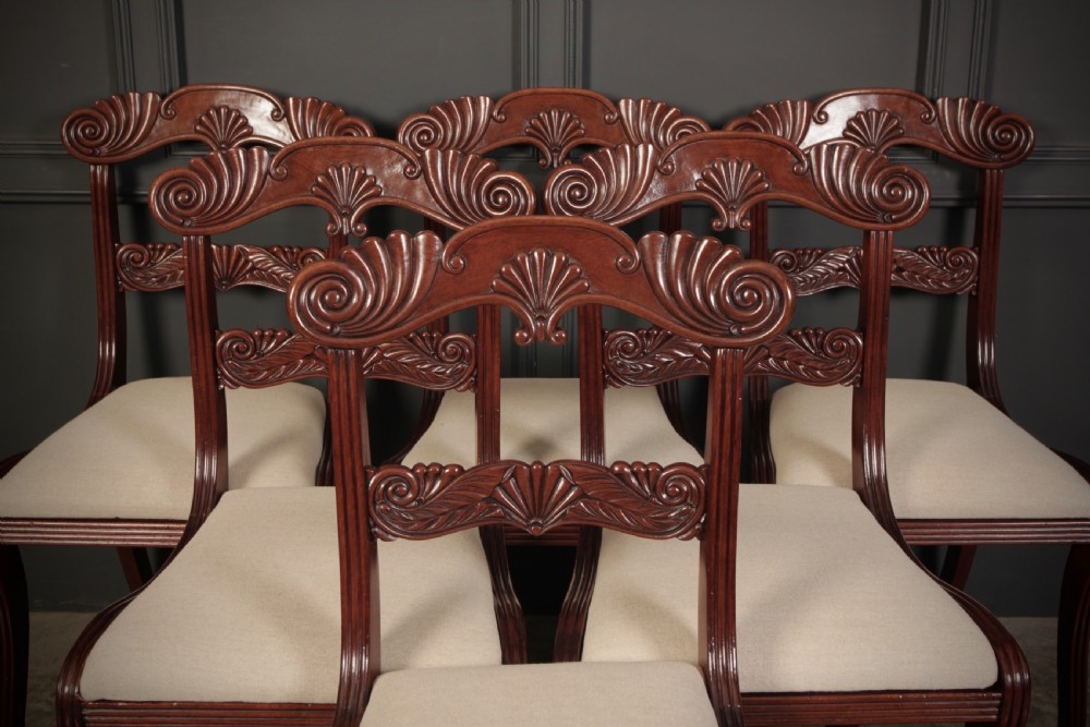 A set of eight carved mahogany Regency dining chairs featuring scroll arms, carved crest rails, and cream upholstered seats. View VI