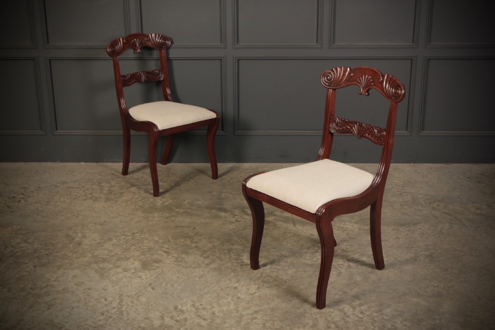 A set of eight carved mahogany Regency dining chairs featuring scroll arms, carved crest rails, and cream upholstered seats. View VII