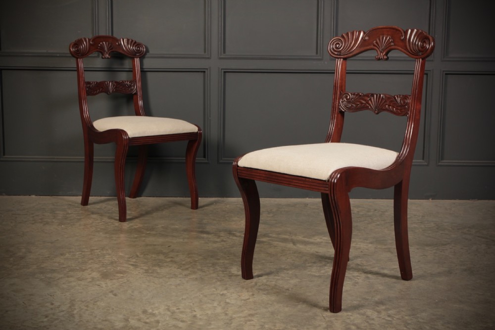 A set of eight carved mahogany Regency dining chairs featuring scroll arms, carved crest rails, and cream upholstered seats. View VIII