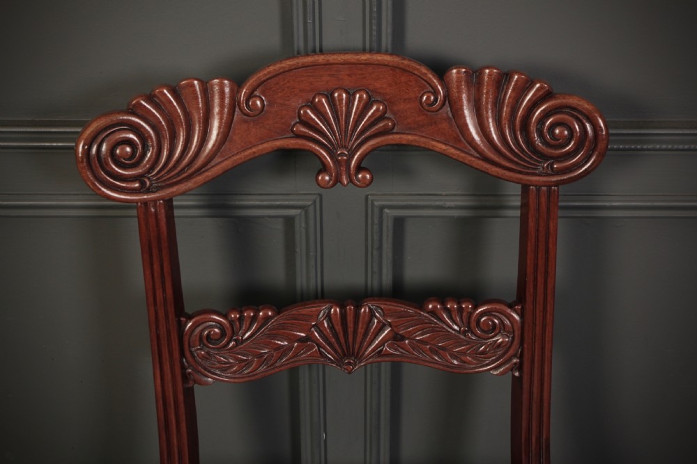 A set of eight carved mahogany Regency dining chairs featuring scroll arms, carved crest rails, and cream upholstered seats. View XII