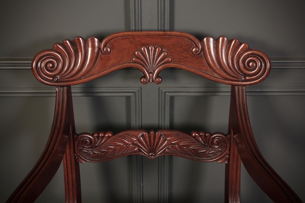 A set of eight carved mahogany Regency dining chairs featuring scroll arms, carved crest rails, and cream upholstered seats. View XVIII