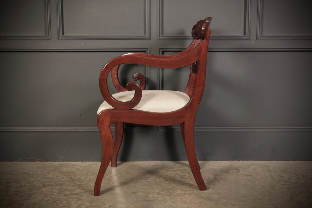 A set of eight carved mahogany Regency dining chairs featuring scroll arms, carved crest rails, and cream upholstered seats. View XXI
