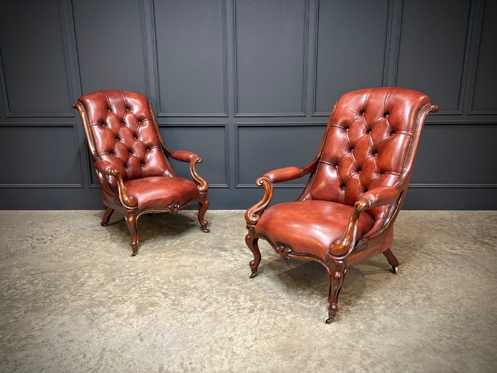 A pair of Victorian library armchairs upholstered in deep-buttoned reddish-brown leather with carved mahogany frames and brass castors. View II