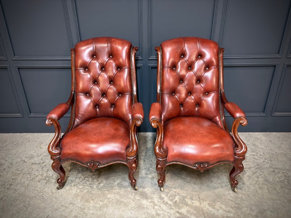 A pair of Victorian library armchairs upholstered in deep-buttoned reddish-brown leather with carved mahogany frames and brass castors. View IV