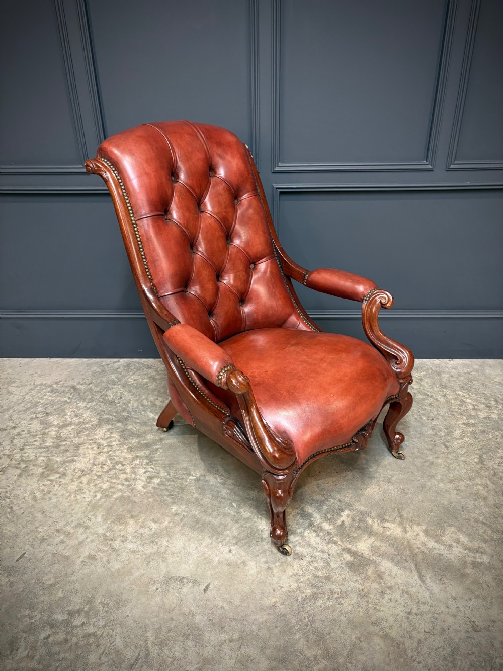 A pair of Victorian library armchairs upholstered in deep-buttoned reddish-brown leather with carved mahogany frames and brass castors. View V