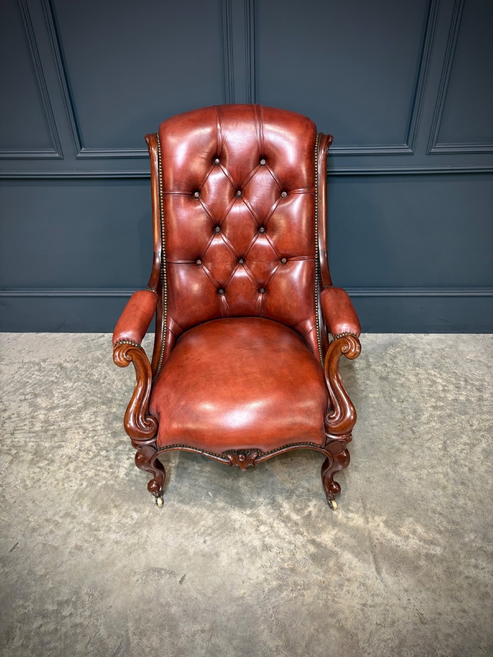 A pair of Victorian library armchairs upholstered in deep-buttoned reddish-brown leather with carved mahogany frames and brass castors. View VII