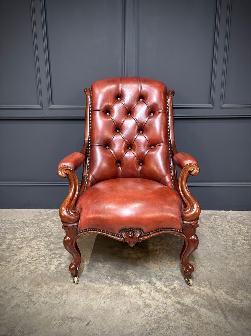 A pair of Victorian library armchairs upholstered in deep-buttoned reddish-brown leather with carved mahogany frames and brass castors. View VIII