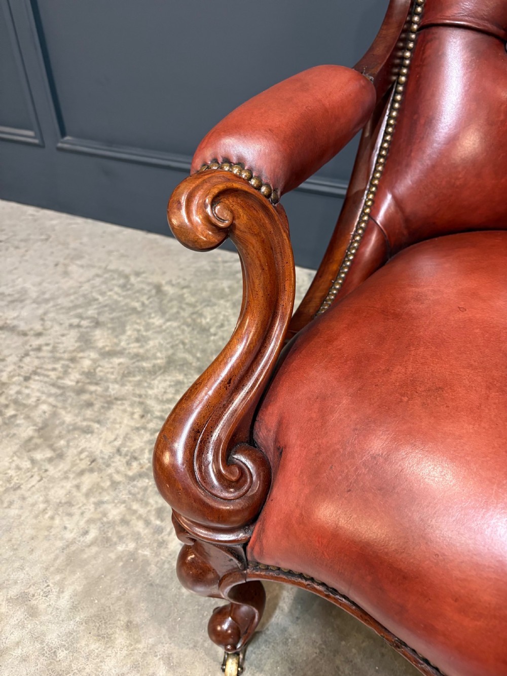 A pair of Victorian library armchairs upholstered in deep-buttoned reddish-brown leather with carved mahogany frames and brass castors. View IX