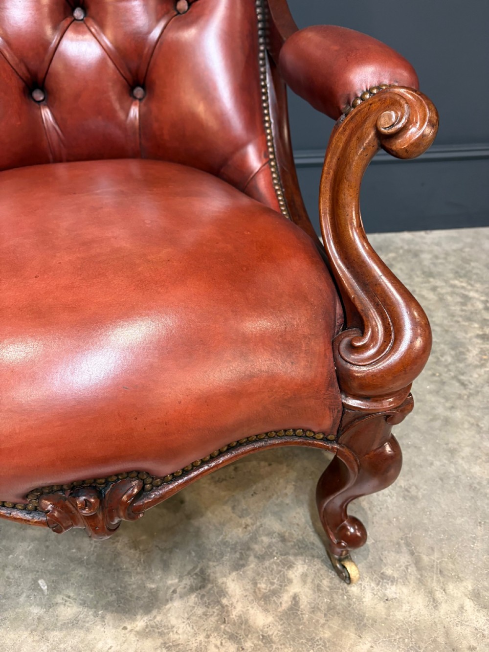A pair of Victorian library armchairs upholstered in deep-buttoned reddish-brown leather with carved mahogany frames and brass castors. View X