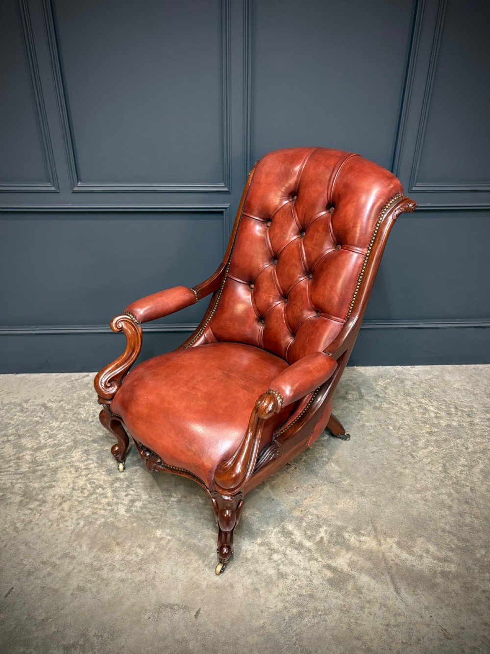 A pair of Victorian library armchairs upholstered in deep-buttoned reddish-brown leather with carved mahogany frames and brass castors. View XI