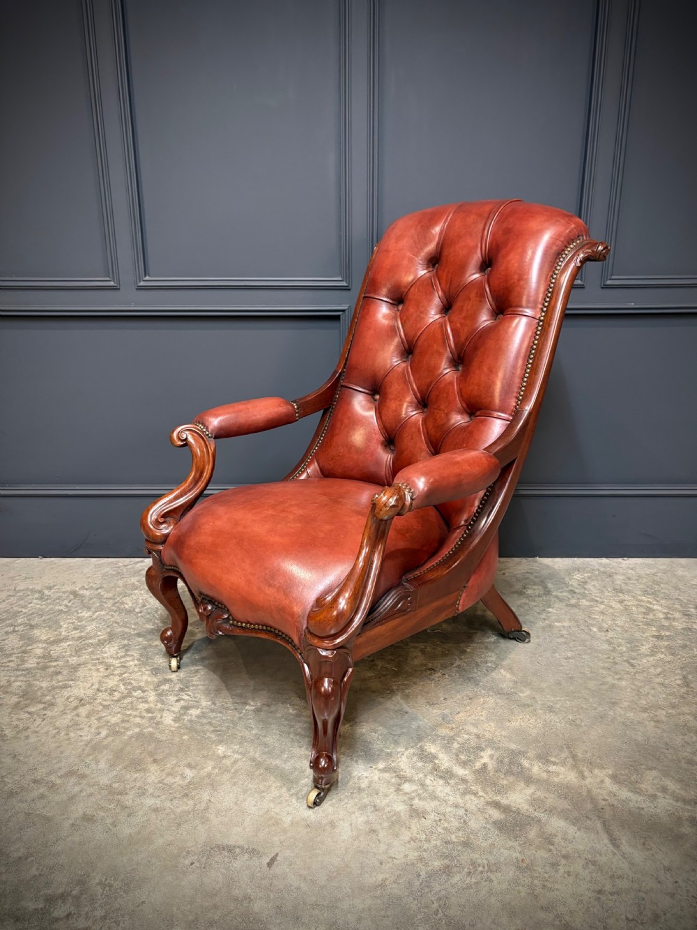 A pair of Victorian library armchairs upholstered in deep-buttoned reddish-brown leather with carved mahogany frames and brass castors. View XII
