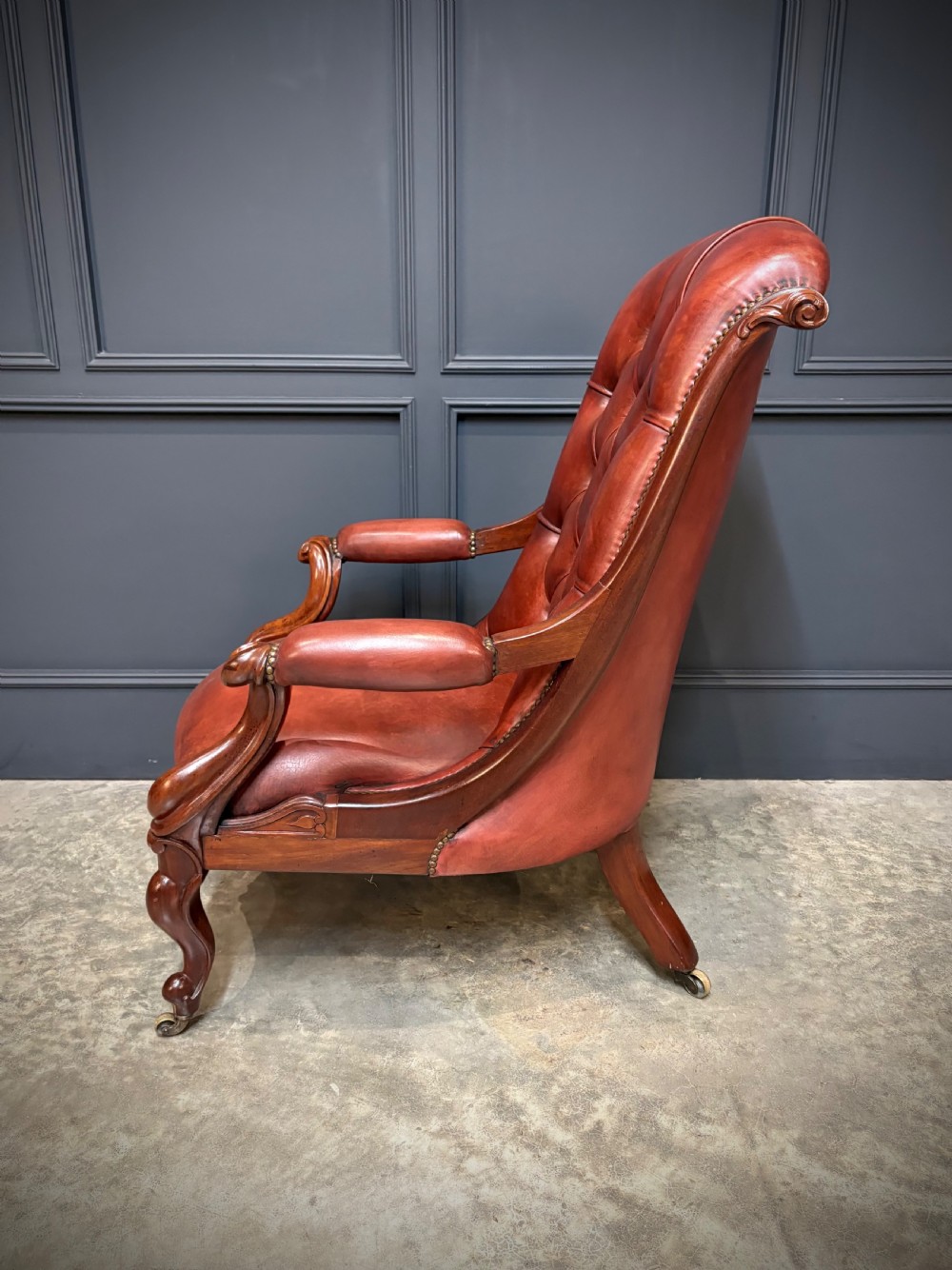A pair of Victorian library armchairs upholstered in deep-buttoned reddish-brown leather with carved mahogany frames and brass castors. View XIII
